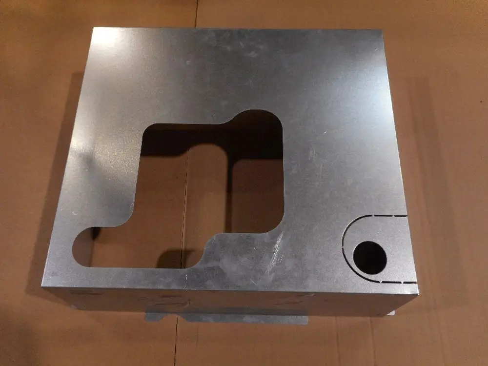Metallische Hinterwand von Remeha mit einer Öffnung und einer runden Aussparung, auf einer braunen Box liegend.